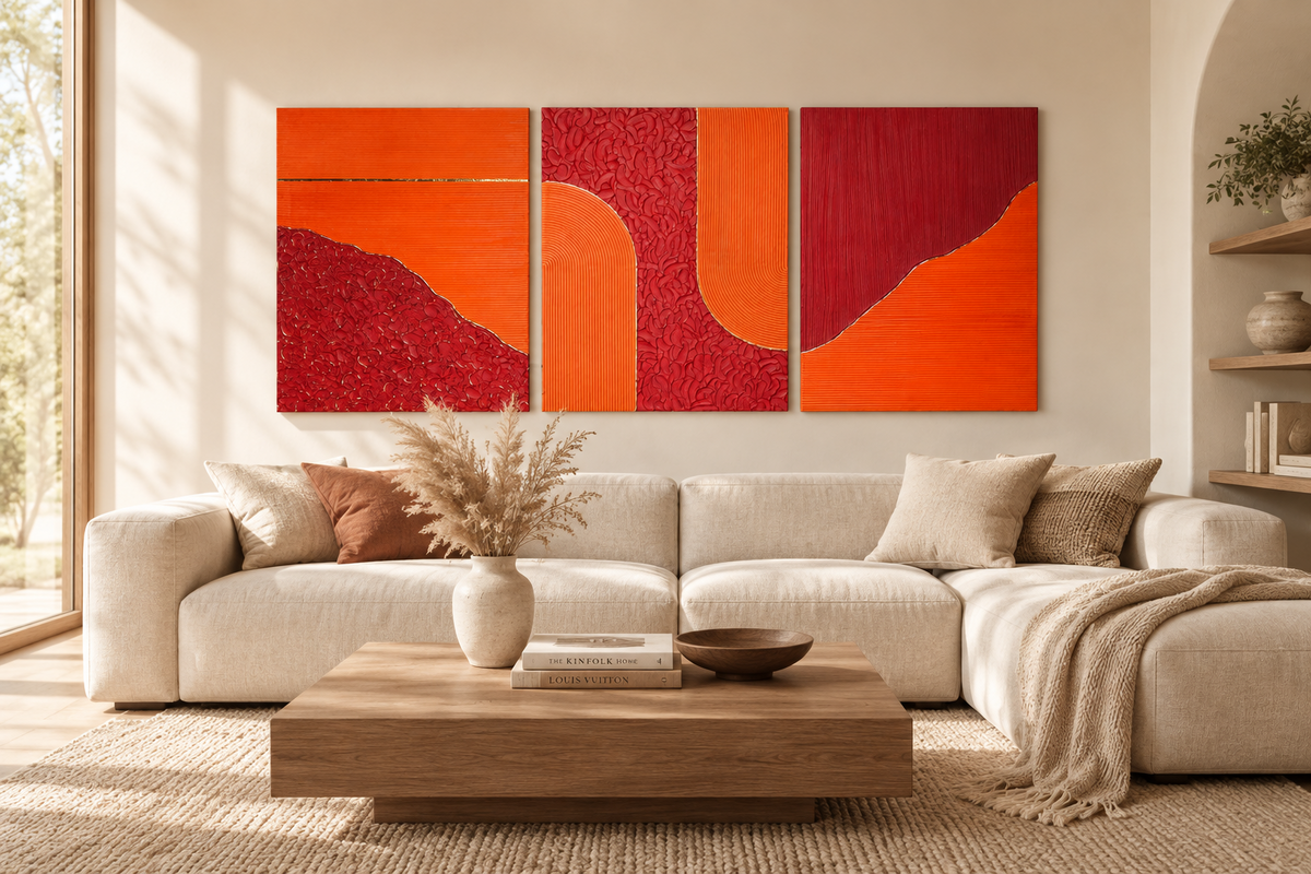 Mise en situation de trois tableaux abstraits texturés orange et bordeaux au-dessus d’un canapé d’angle dans un salon lumineux.